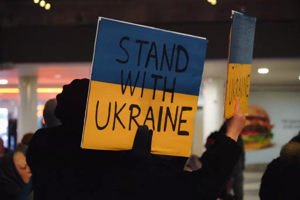 Protestor holds sign in Ukrainian colours with the text stand with Ukraine.