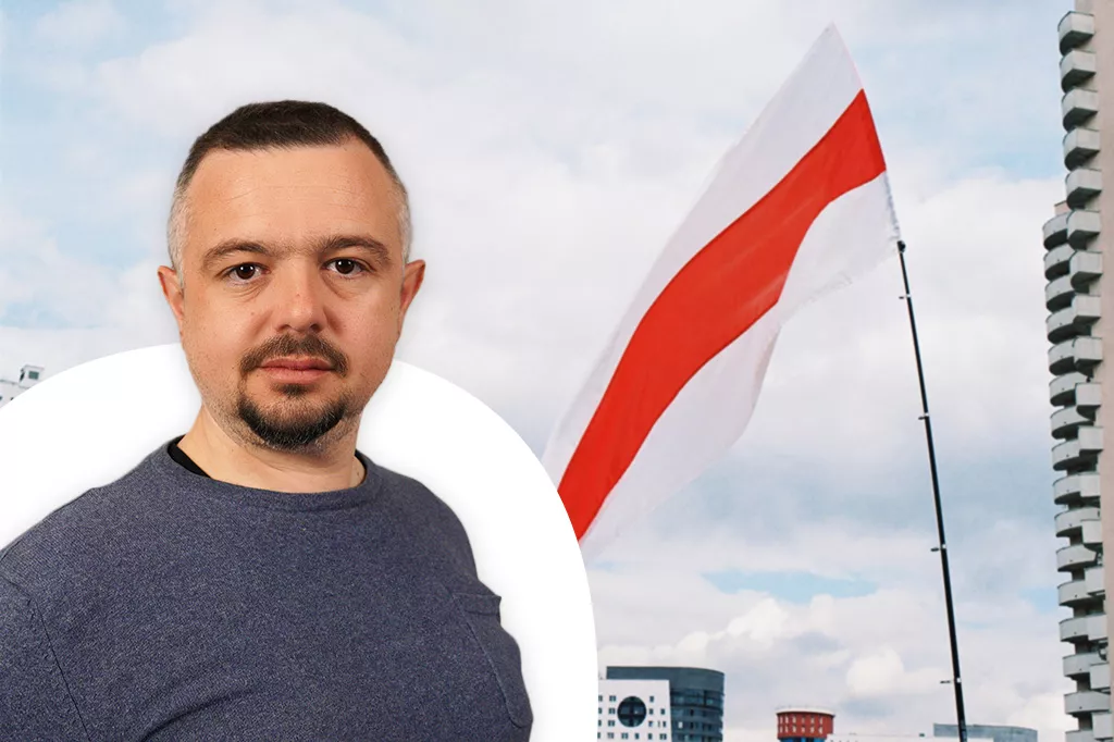 Ognjen looks into the camera. He is wearing a blue sweater. Behind him is a Belarusian flag. 