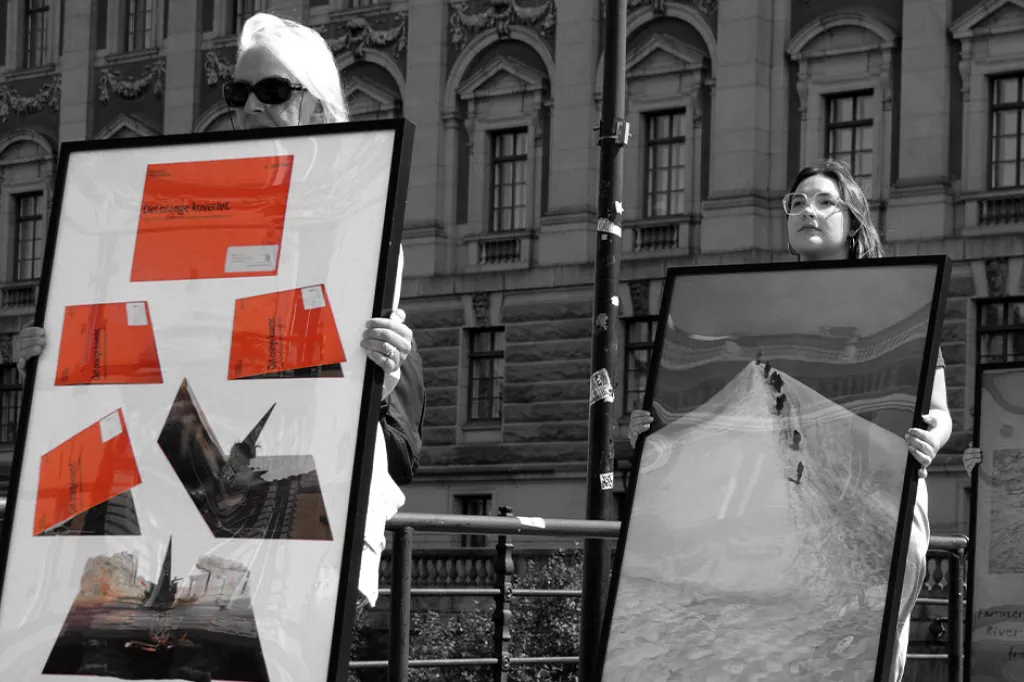 Två personer går med inramade konstverket om AP-fonderna utanför riksdagen.