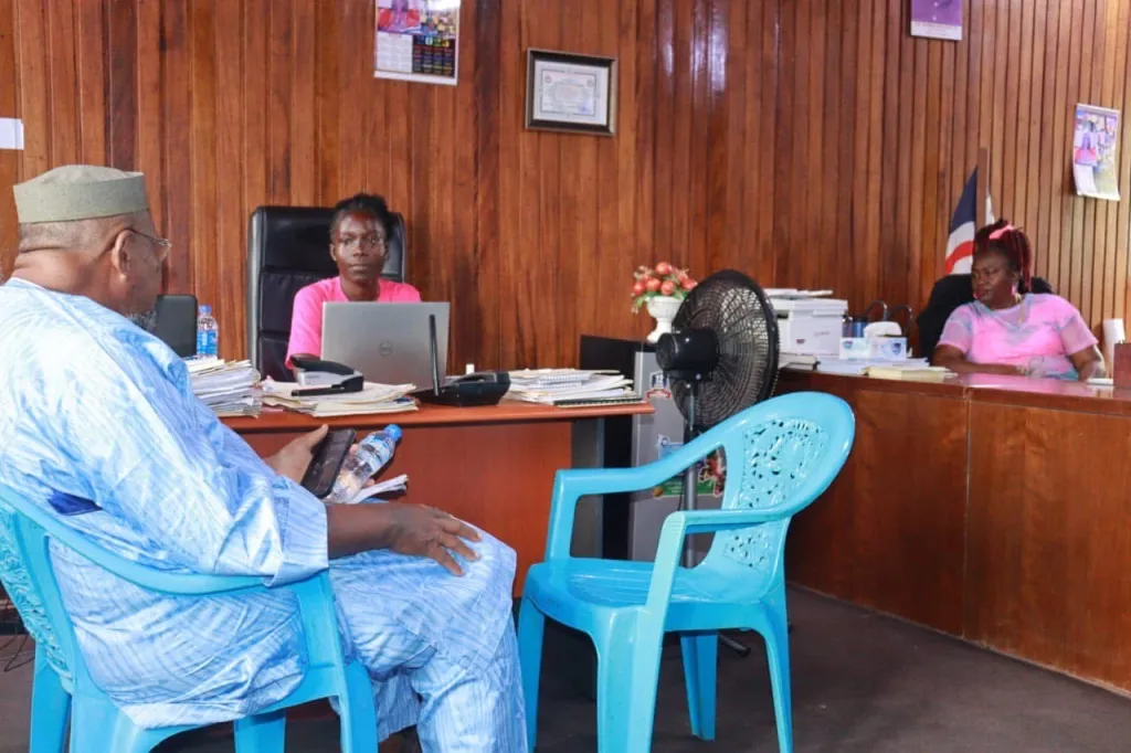 Two women in pink t-shirts are sitting at desks in a government office. 