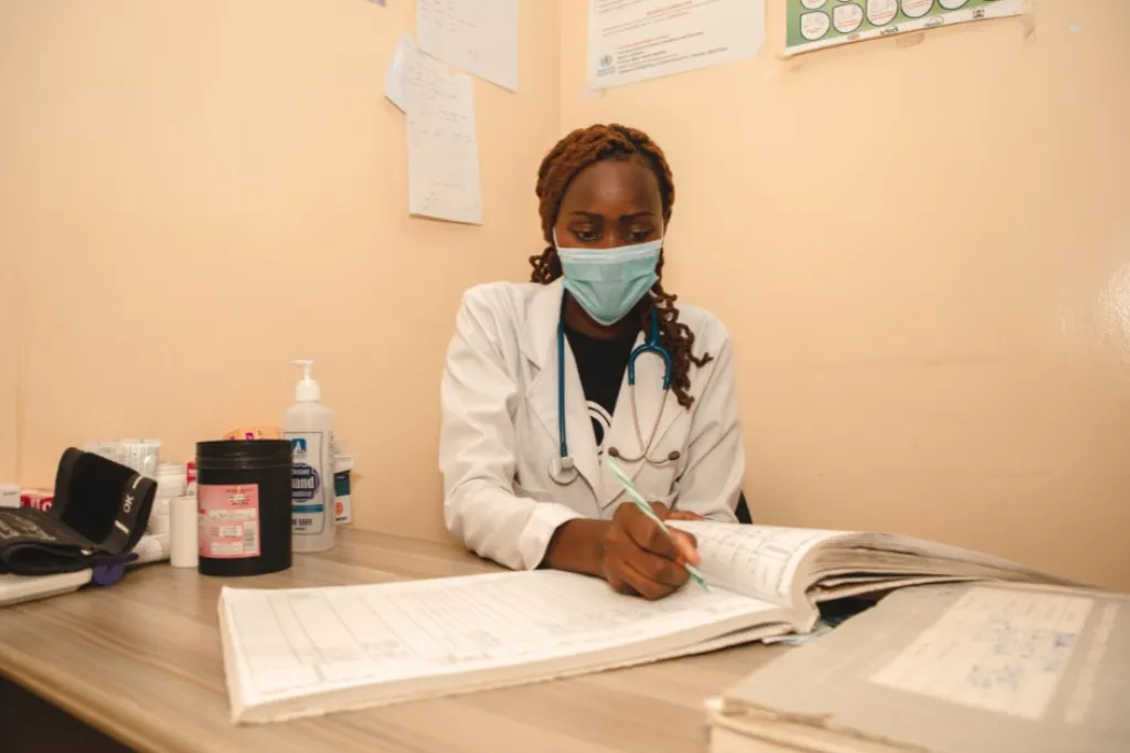 Nurse wearing a face mask and writing in a ledger. 