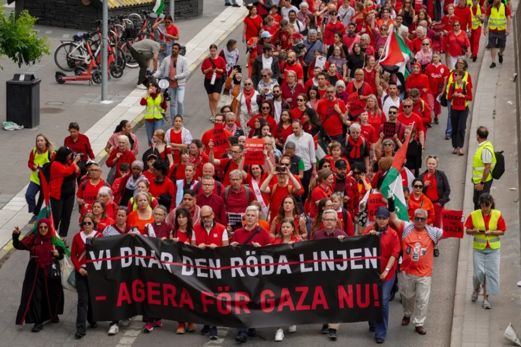 Tåg med människor klädda i rött på Sveavägen i Stockholm. Banderoll med texten vi drar den röda linjen, agera för gaza nu