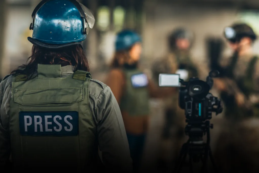 Journalist wearing a protective vest with the text press and a blue helmet.