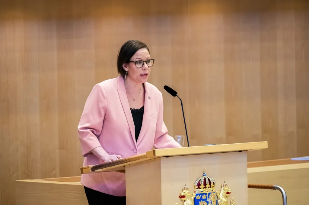 Maria Malmer Stenergard i talarstolen i Riksdagen iklädd en rosa kavaj.