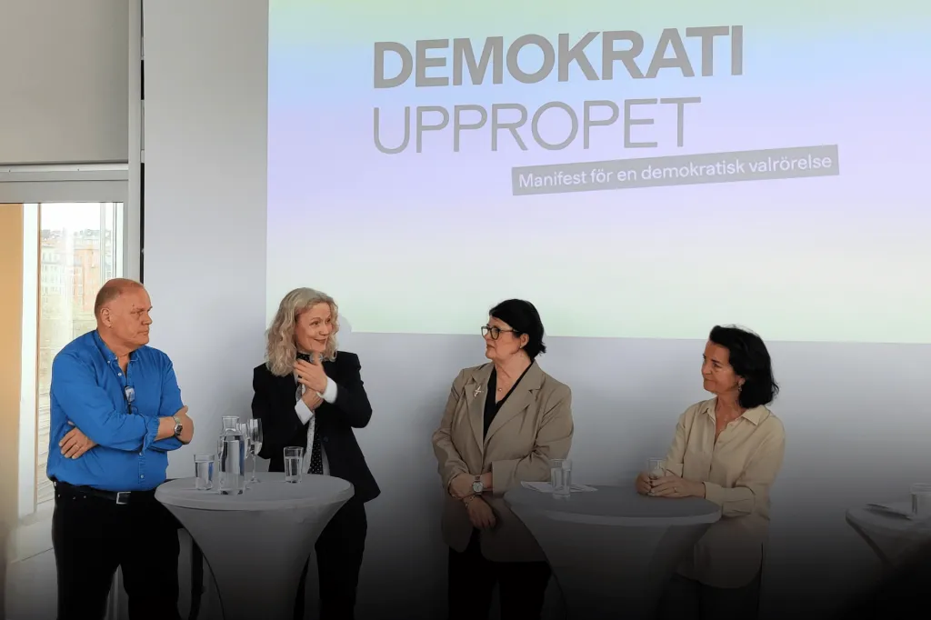 Göran, Åsa, Heike och Anna talar vid runda ståbord. I bakgrunden syns texten demokratiuppropet.