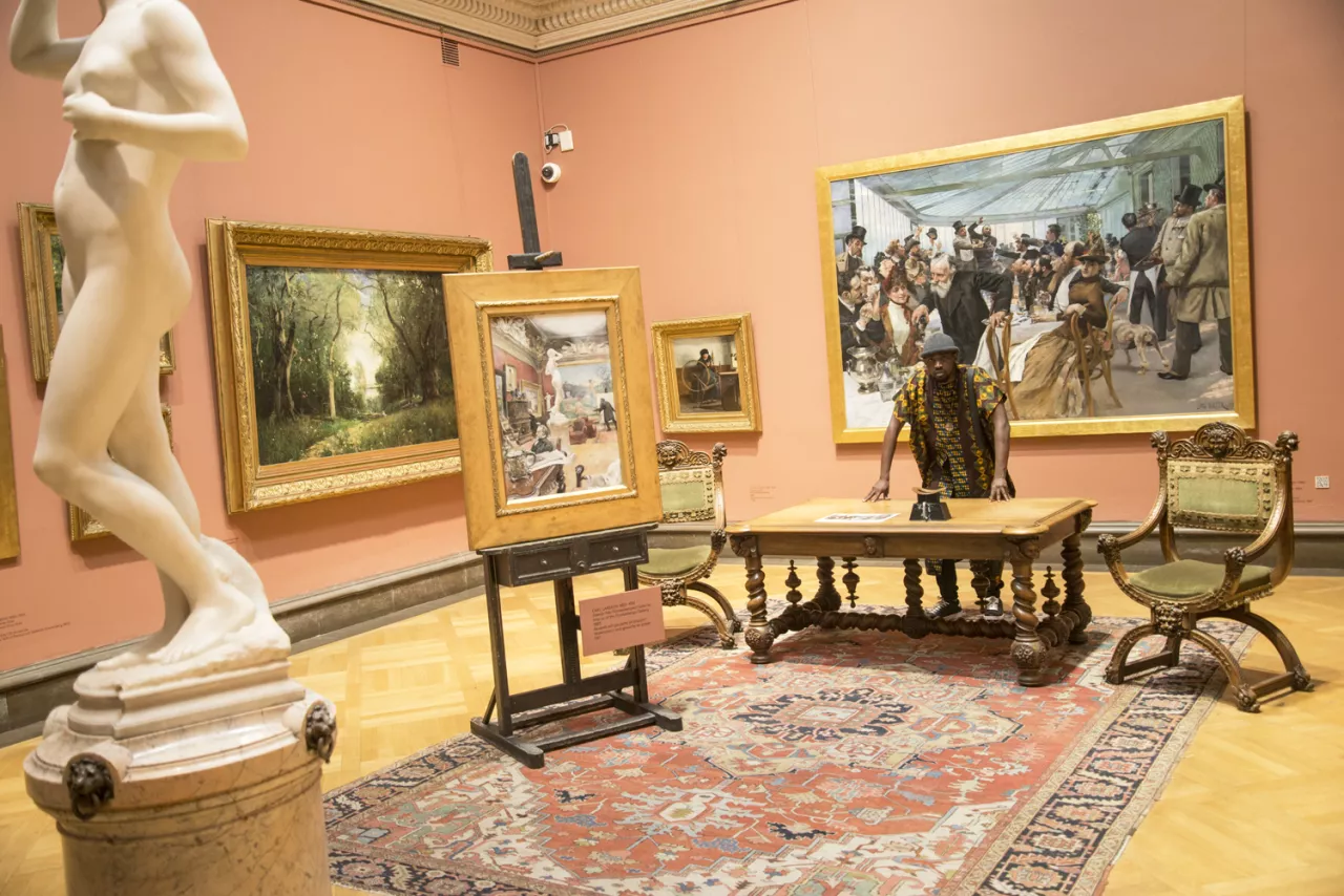 Mufasa står i ett rum fyllt med konst från svenska konstnärer. 