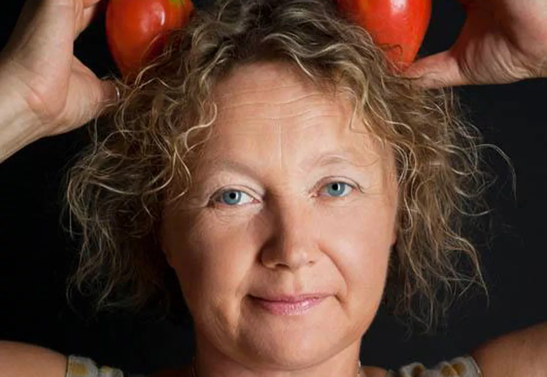 Irina håller två tomater ovanför huvudet mot en svart bakgrund.