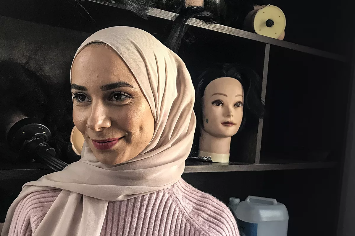 Porträtt av Doaa i hijab och ribbad tröja. I bakgrunden ser man huvuden som man övar för att sminka på.