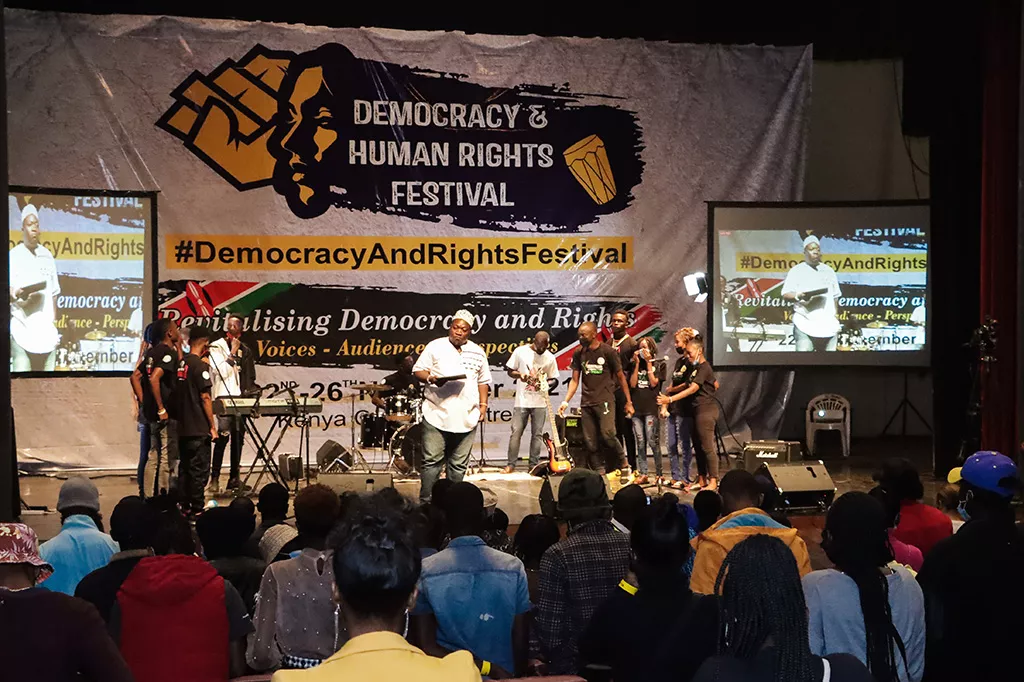 Människor i Kenya står på scen framför en publik. I bakgrund syns en banderoll med texten democracy and human rights festival.