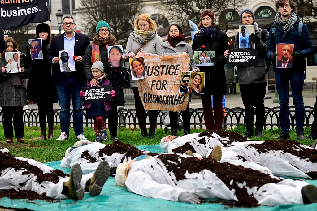 Demonstranter står med skyltar med texten justice for Brumadinho. I förgrunden ligger fyra personer täckta med jord.