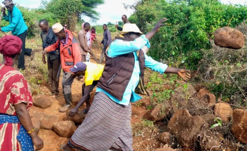 People clearing stones from a dirt road in Kenya.