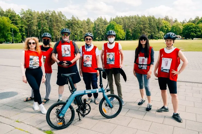 Seven people staning on a road with red shirts on with pictures of journalists