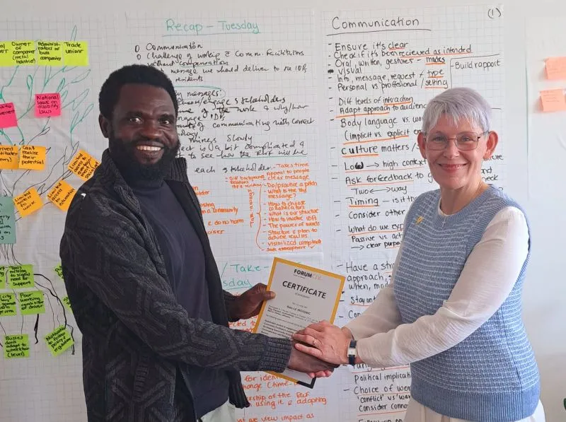 Two people shaking hans in front of white board