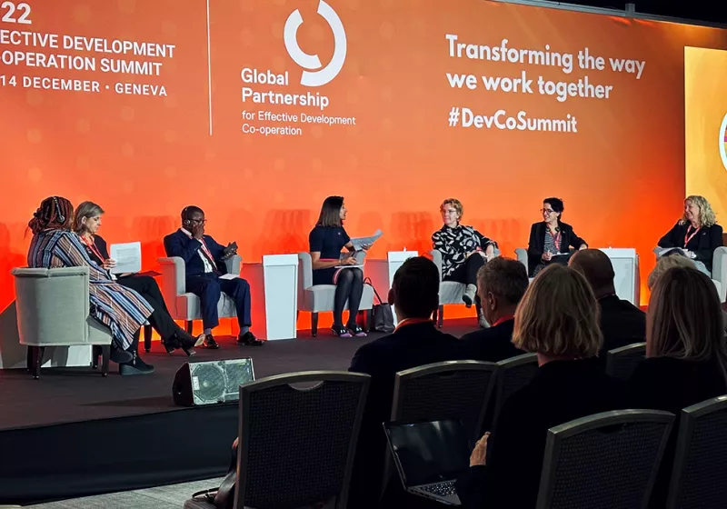 Deltagare sitter på en stor scen med orange bakgrund där det står transforming the way we work together.