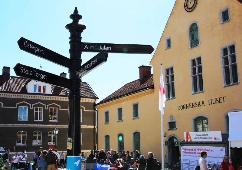 A photo of a yellow building with the text Donnerska huset. On the left side there is a street sign that says Almedalen.