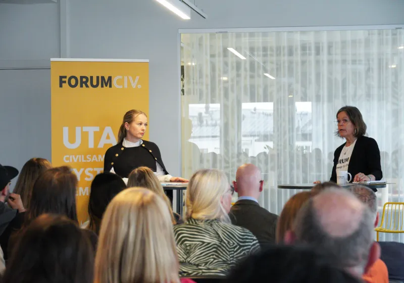 Diana Janse står framför en gul roll-up med ForumCivs logotyp. Till höger står Anna Stenvinkel.