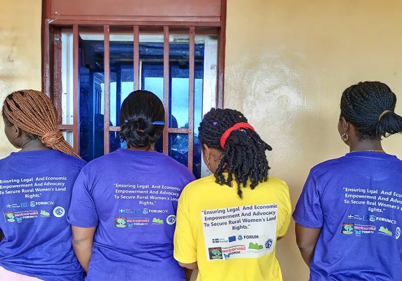 4 women have their back against the camera to show the text Empowering Rural Women through Legal and Economic Advocacy for Land Rights written on their purple t-shirts.