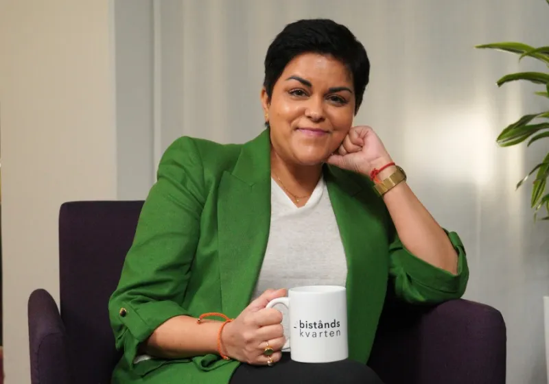Parul iklädd grön kavaj sitter i en fåtölj