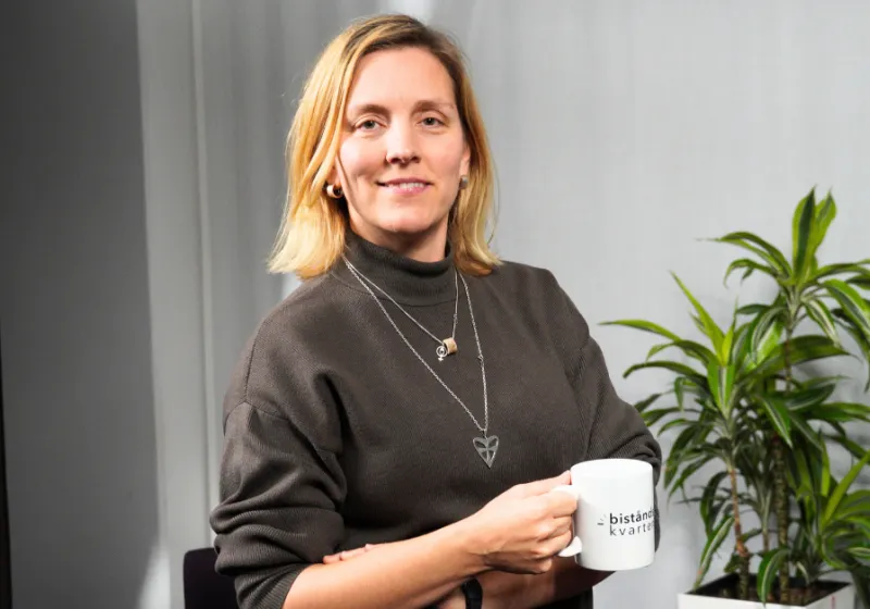 Anna håller en kaffekopp iklädd en brun polotröja