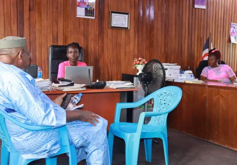 Two women in pink t-shirts are sitting at desks in a government office. 