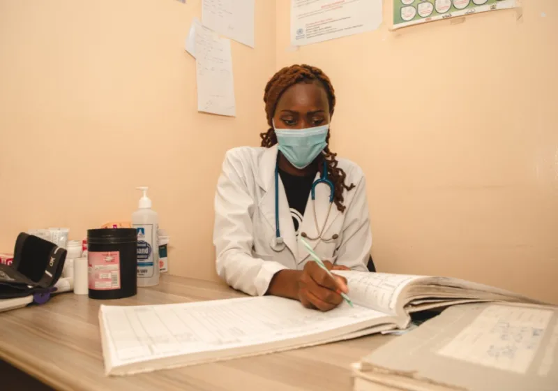 Nurse wearing a face mask and writing in a ledger. 