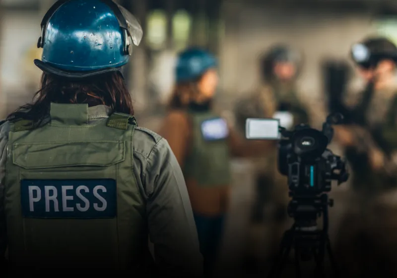 Journalist wearing a protective vest with the text press and a blue helmet.