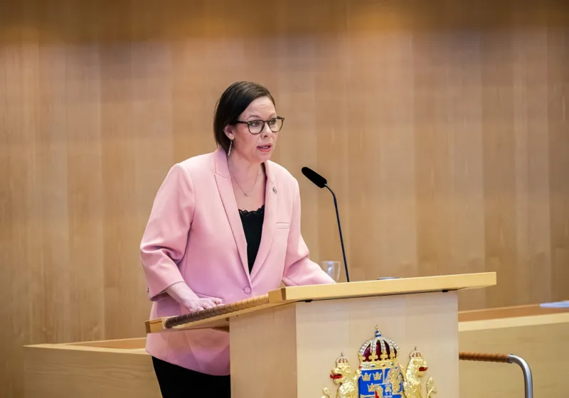 Maria Malmer Stenergard i talarstolen i Riksdagen iklädd en rosa kavaj.