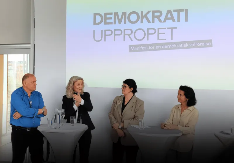 Göran, Åsa, Heike och Anna talar vid runda ståbord. I bakgrunden syns texten demokratiuppropet.