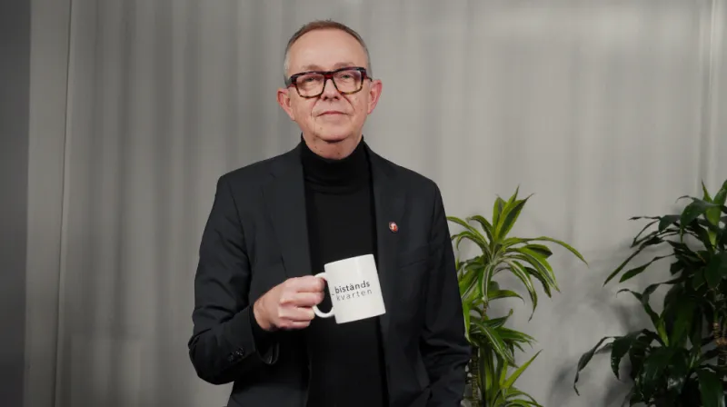 Anders i svart polo och grå kavaj ler mot kameran och håller en vit kopp med texten biståndskvarten.