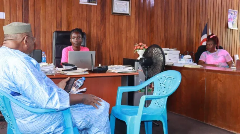 Two women in pink t-shirts are sitting at desks in a government office. 