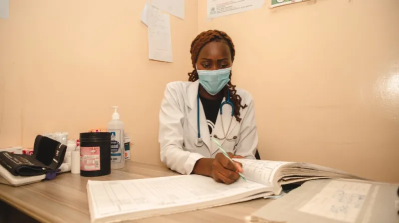 Nurse wearing a face mask and writing in a ledger. 