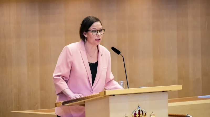 Maria Malmer Stenergard i talarstolen i Riksdagen iklädd en rosa kavaj.