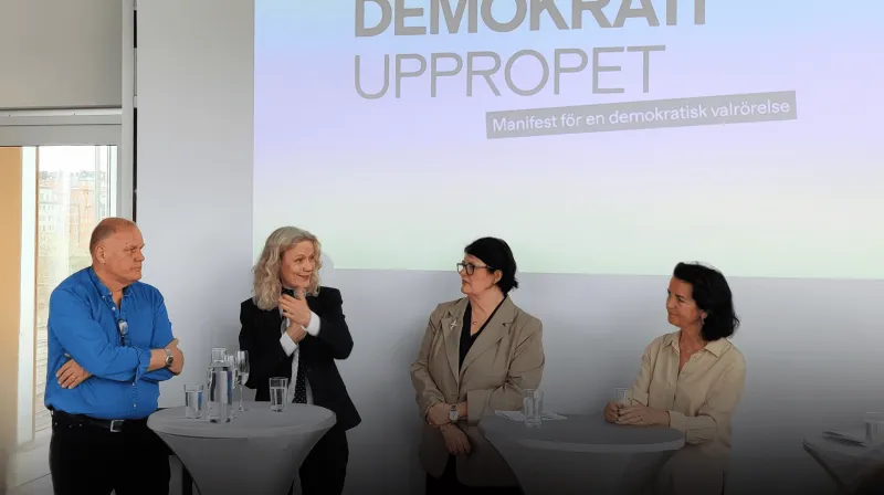 Göran, Åsa, Heike och Anna talar vid runda ståbord. I bakgrunden syns texten demokratiuppropet.