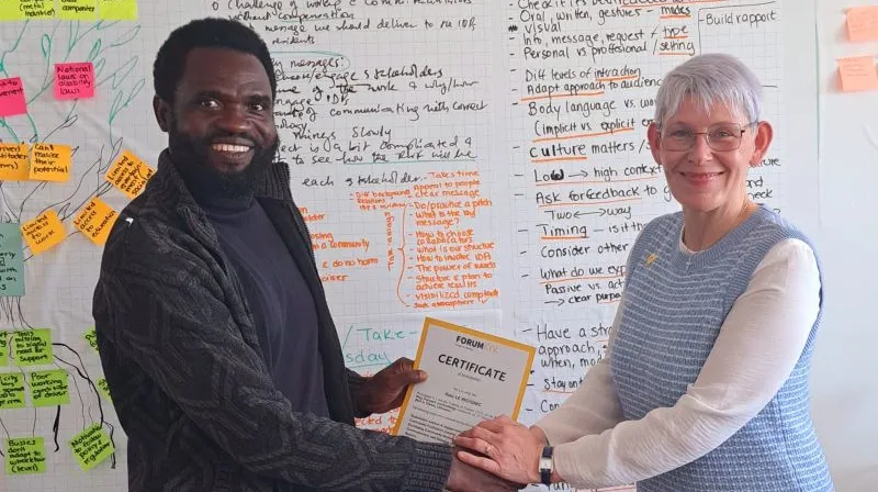 Two people shaking hans in front of white board