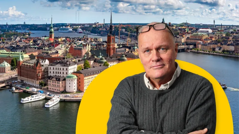 Göran i grå tröja. Bakom honom ett flygfoto över gamla stan i Stockholm. 